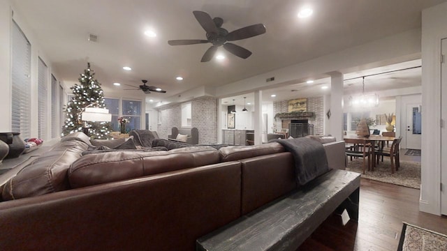 living room featuring ceiling fan with notable chandelier, dark hardwood / wood-style flooring, and a stone fireplace