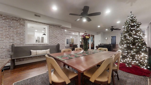 dining room with ceiling fan, dark hardwood / wood-style flooring, and brick wall