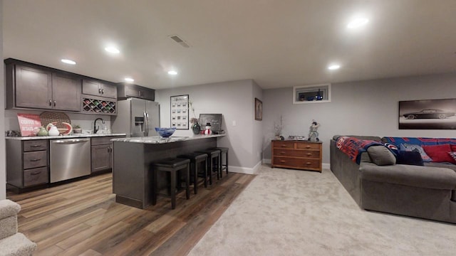 interior space with hardwood / wood-style floors, sink, appliances with stainless steel finishes, dark brown cabinets, and a kitchen bar