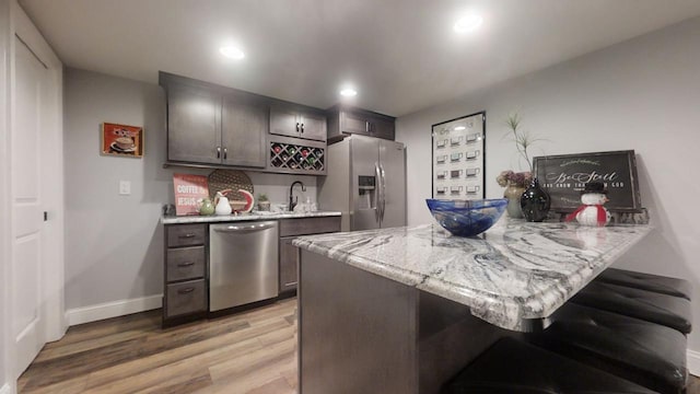 kitchen with kitchen peninsula, appliances with stainless steel finishes, light stone countertops, dark brown cabinetry, and light hardwood / wood-style floors