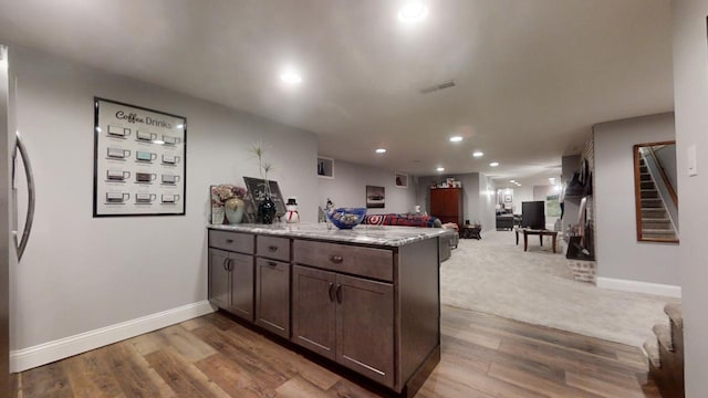 kitchen featuring light stone counters, carpet floors, kitchen peninsula, and dark brown cabinetry