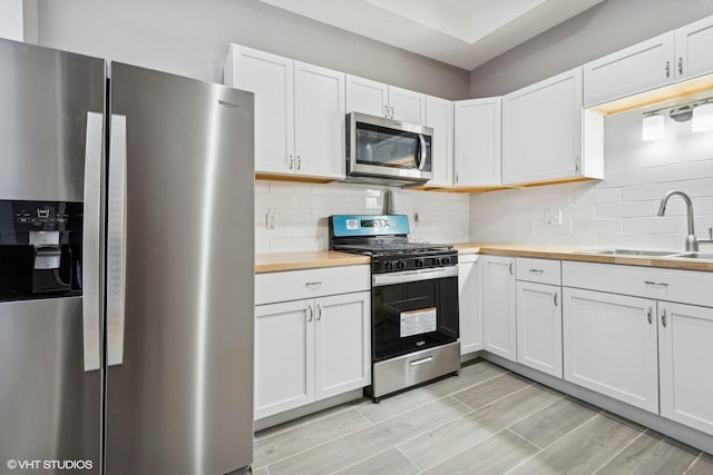 kitchen with butcher block countertops, stainless steel appliances, white cabinetry, and sink