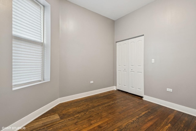 unfurnished bedroom with multiple windows, a closet, and dark hardwood / wood-style floors