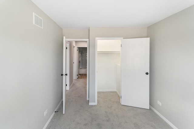 unfurnished bedroom with a spacious closet, light carpet, and a closet