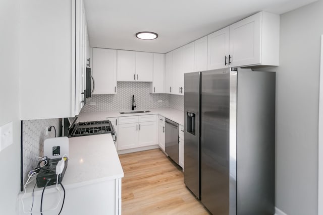 kitchen featuring sink, light hardwood / wood-style floors, decorative backsplash, white cabinets, and appliances with stainless steel finishes