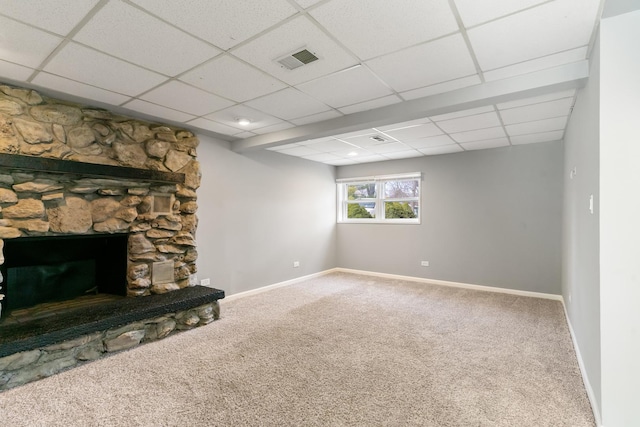 living room featuring carpet floors, a stone fireplace, and a drop ceiling