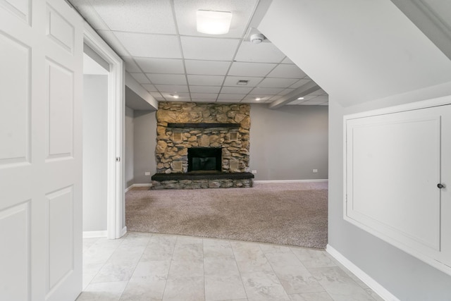 unfurnished living room with a paneled ceiling, a stone fireplace, and light carpet