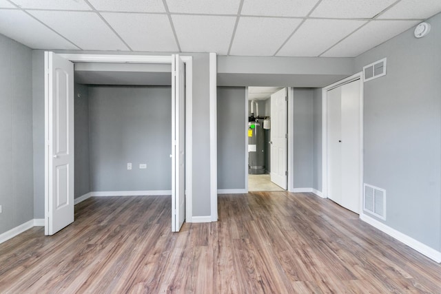 basement with a paneled ceiling, wood-type flooring, and water heater