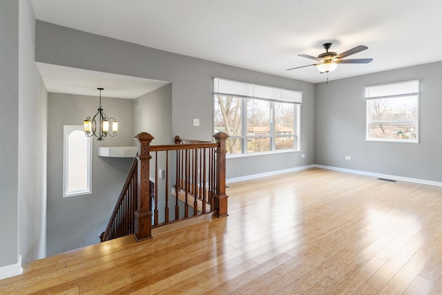 spare room featuring ceiling fan with notable chandelier and light wood-type flooring