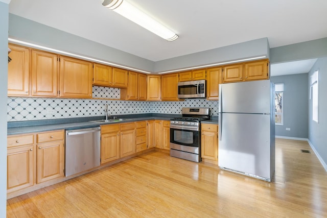 kitchen with appliances with stainless steel finishes, tasteful backsplash, light hardwood / wood-style floors, and sink