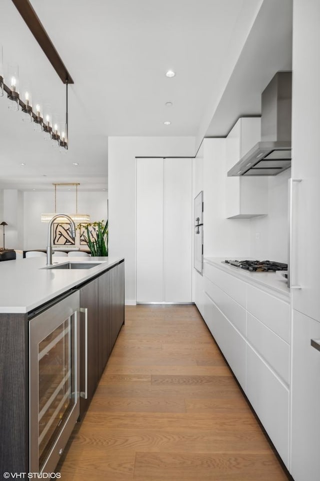 kitchen featuring wine cooler, wall chimney exhaust hood, dark brown cabinets, white cabinetry, and hanging light fixtures