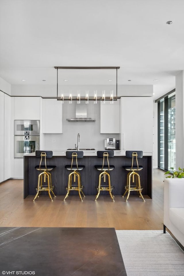 kitchen featuring white cabinets, decorative light fixtures, a kitchen bar, and wood-type flooring