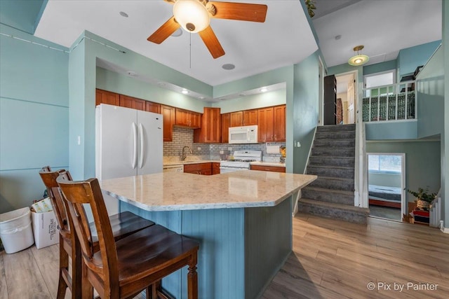 kitchen featuring backsplash, ceiling fan, white appliances, and light wood-type flooring