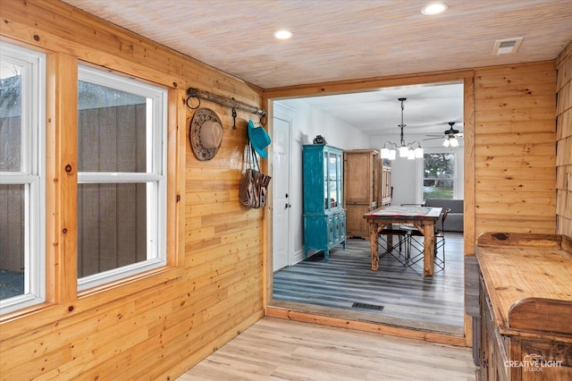 dining space with wood ceiling, ceiling fan with notable chandelier, light hardwood / wood-style flooring, and wooden walls