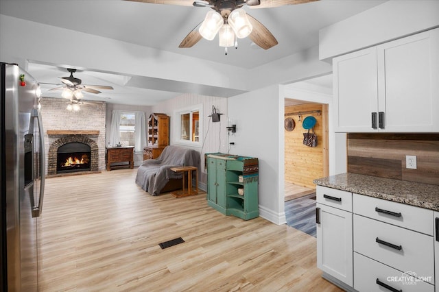 kitchen with stainless steel fridge with ice dispenser, a brick fireplace, light wood-type flooring, white cabinets, and stone countertops