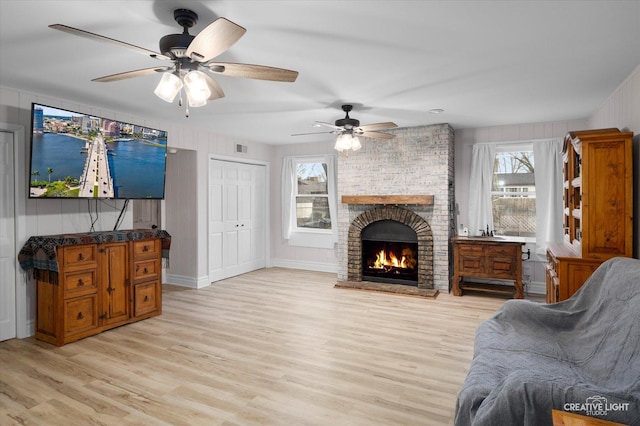 living room with light hardwood / wood-style floors, a wealth of natural light, ceiling fan, and a fireplace