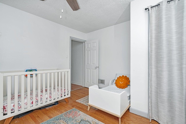 bedroom with a crib, hardwood / wood-style floors, a textured ceiling, and ceiling fan