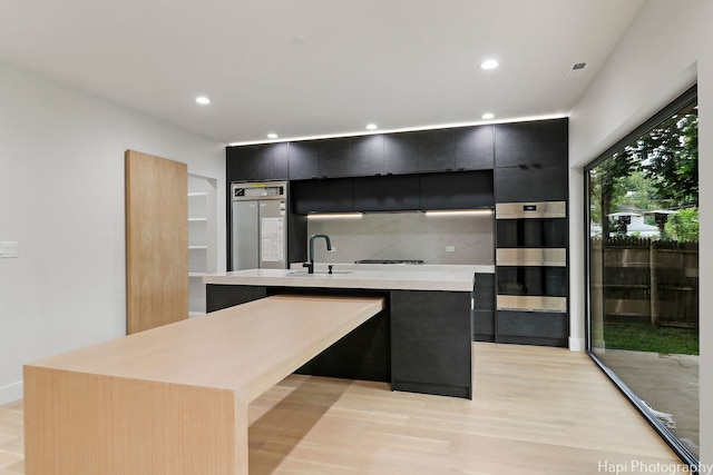 kitchen featuring a center island with sink, decorative backsplash, sink, and light hardwood / wood-style flooring