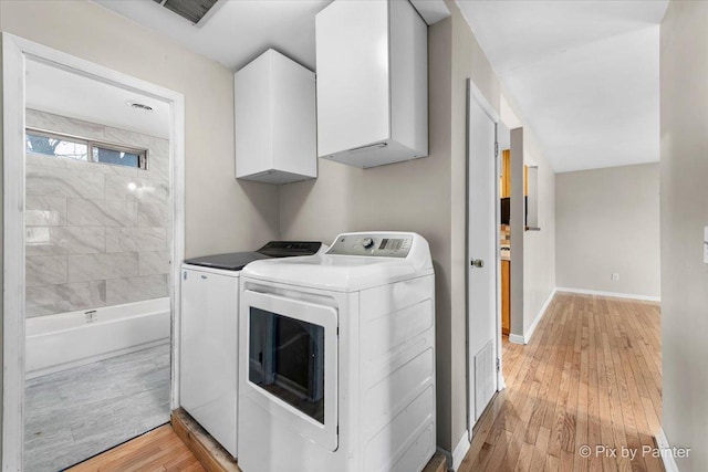 washroom featuring washer and dryer, light hardwood / wood-style floors, and cabinets