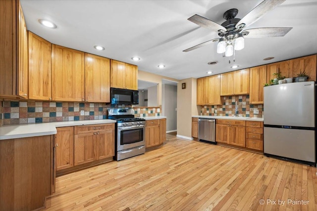 kitchen featuring sink, decorative backsplash, ceiling fan, light wood-type flooring, and appliances with stainless steel finishes