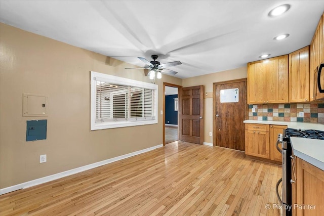 kitchen featuring electric panel, stainless steel gas stove, ceiling fan, decorative backsplash, and light wood-type flooring