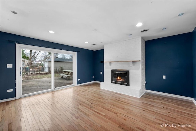 unfurnished living room with a brick fireplace and light hardwood / wood-style flooring