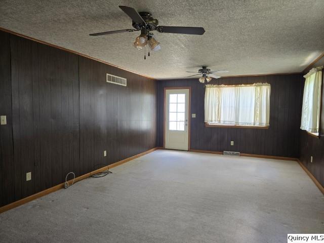 empty room with ceiling fan, wood walls, light carpet, and a textured ceiling