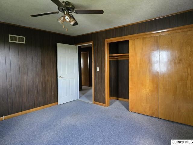 unfurnished bedroom featuring a closet, carpet floors, ceiling fan, and wood walls