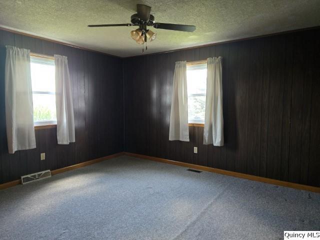 carpeted spare room featuring ceiling fan, wooden walls, and a textured ceiling