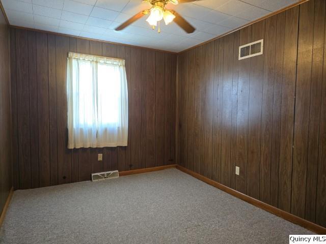 carpeted empty room with ceiling fan and wood walls