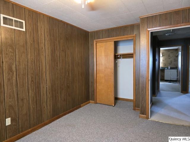 unfurnished bedroom featuring ceiling fan, light colored carpet, a closet, and wood walls