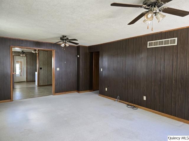 spare room with ceiling fan, light colored carpet, wooden walls, and a textured ceiling