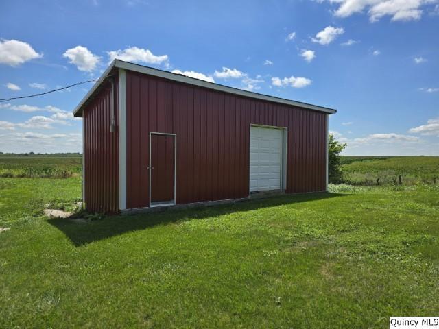 view of outdoor structure with a garage, a lawn, and a rural view