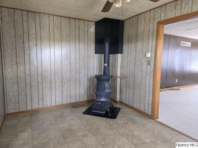 interior details with wooden walls, ceiling fan, and a wood stove