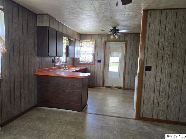 kitchen featuring ceiling fan, dark brown cabinets, sink, and wooden walls