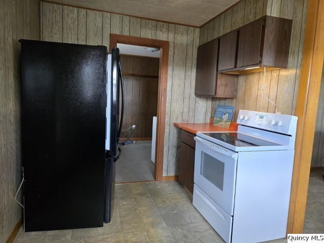 kitchen featuring wood walls, white electric range oven, and black fridge