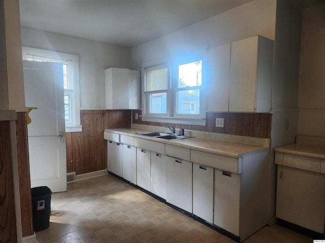 kitchen with white cabinetry, sink, and wood walls