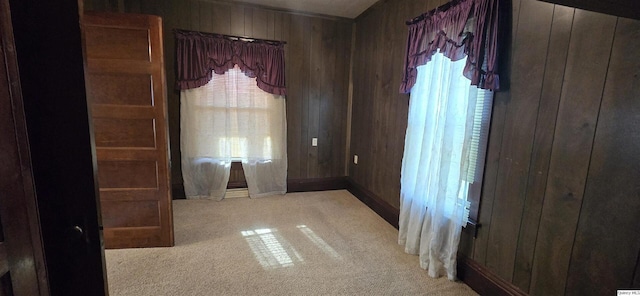 empty room featuring plenty of natural light, light colored carpet, and wooden walls