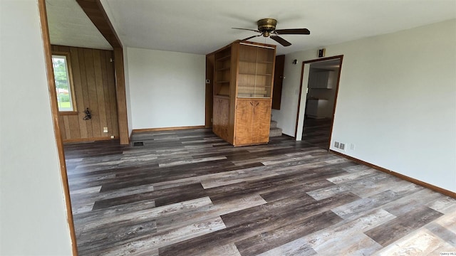 interior space with wooden walls, dark hardwood / wood-style floors, and ceiling fan