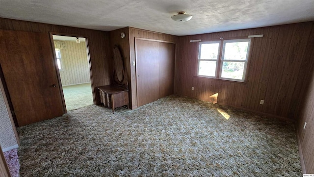 unfurnished bedroom with wood walls, a closet, a textured ceiling, and carpet flooring