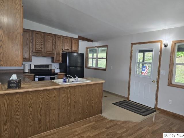 kitchen with stainless steel electric stove, black refrigerator, sink, kitchen peninsula, and light wood-type flooring