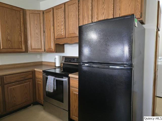 kitchen featuring stainless steel electric range oven, washer / dryer, and black refrigerator