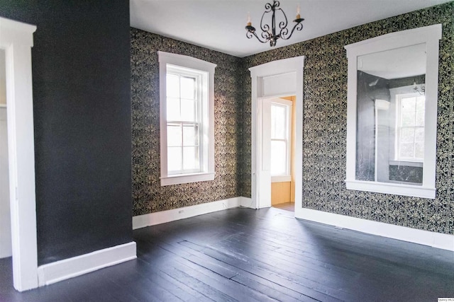 empty room with a notable chandelier and dark hardwood / wood-style flooring