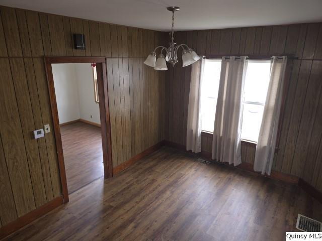 unfurnished dining area with a notable chandelier, dark wood-type flooring, and wood walls