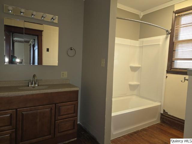 bathroom with washtub / shower combination, ornamental molding, wood-type flooring, and vanity