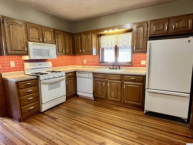 kitchen featuring sink, decorative backsplash, white appliances, a textured ceiling, and light hardwood / wood-style flooring