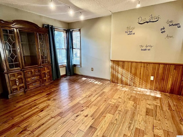 spare room with hardwood / wood-style floors, wooden walls, rail lighting, and a textured ceiling