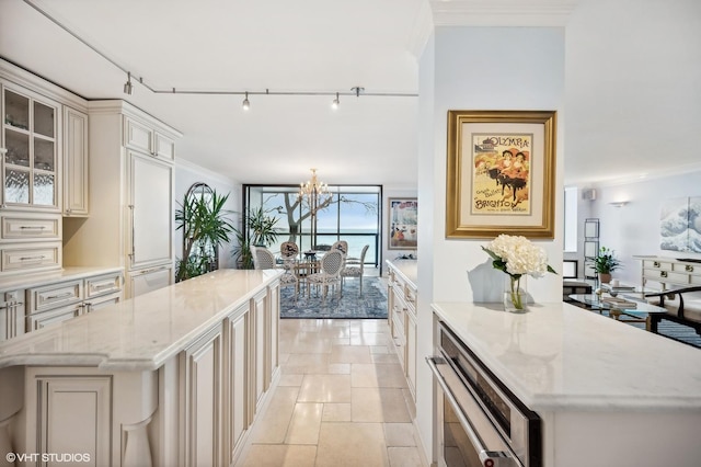 kitchen with light stone counters, crown molding, a center island, a notable chandelier, and cream cabinets