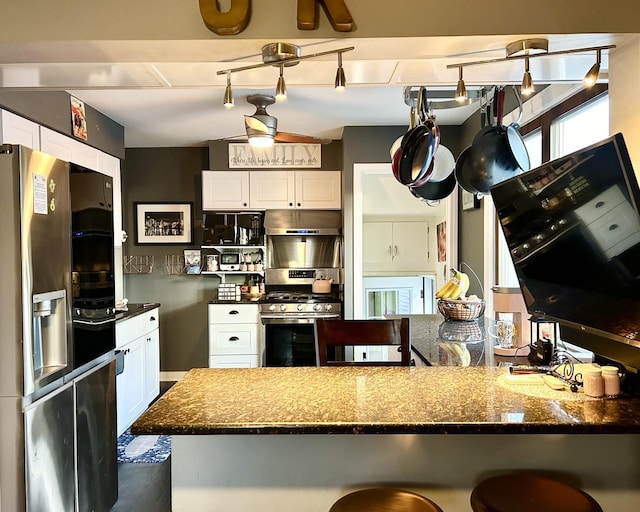 kitchen with white cabinetry, ceiling fan, stainless steel appliances, dark stone counters, and a kitchen bar