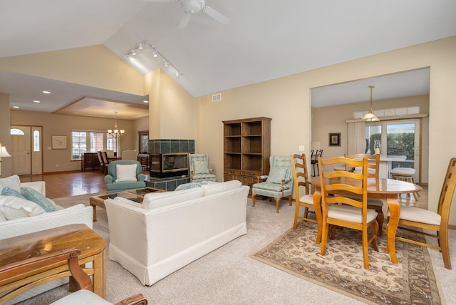 carpeted living room featuring lofted ceiling, a fireplace, and ceiling fan with notable chandelier